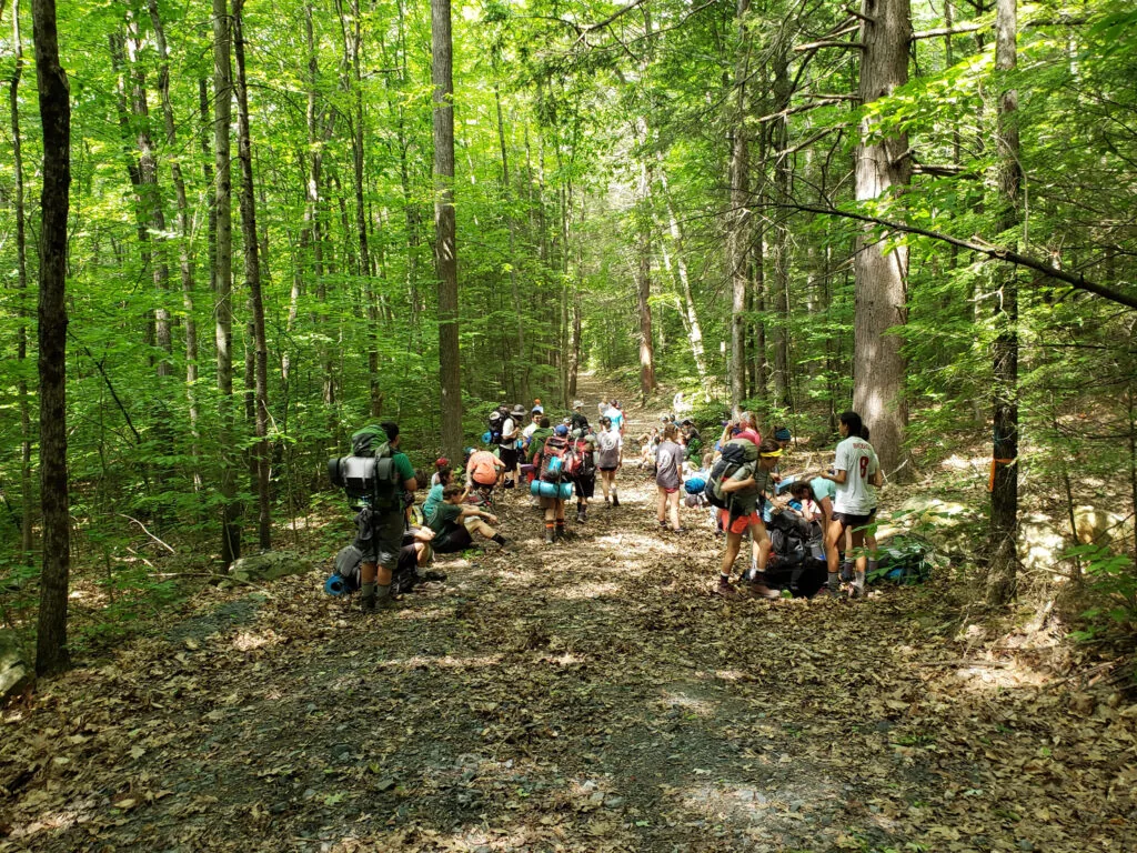 Survival participants with backpacks gathered along a forest trail
